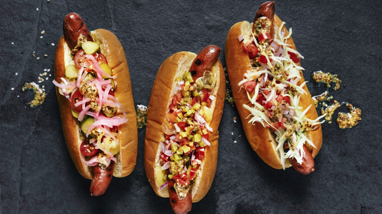 Hot dogs in buns with vegetable toppings on black background