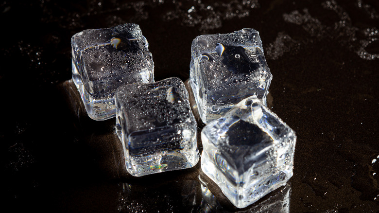 Four clear ice cubes on black surface