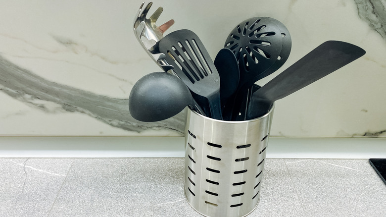 A metal utensil holder sits on a kitchen counter