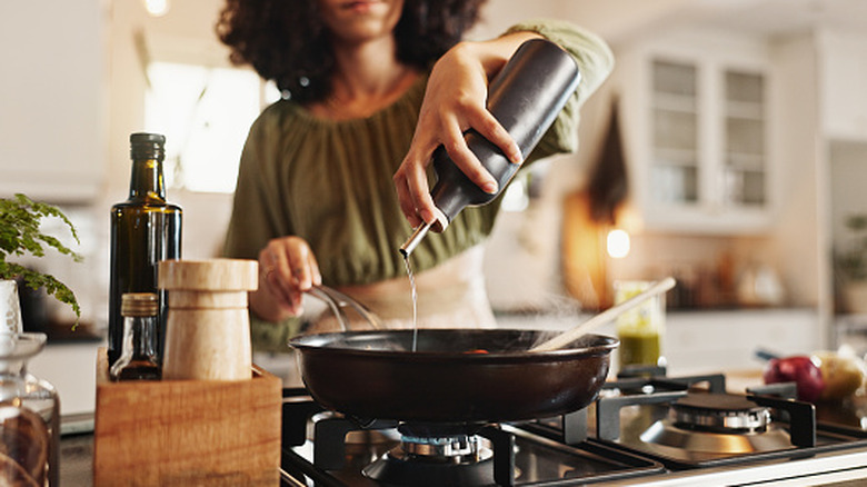 A person cooking and pouring oil into a steaming pan.