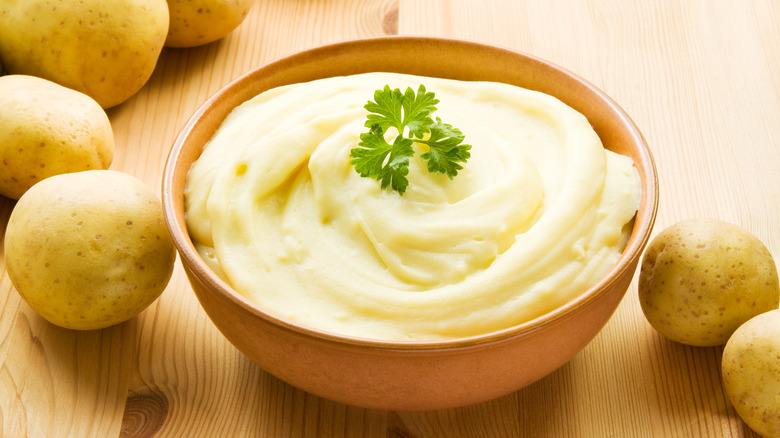 Mashed potatoes in bowl surrounded by raw whole potatoes