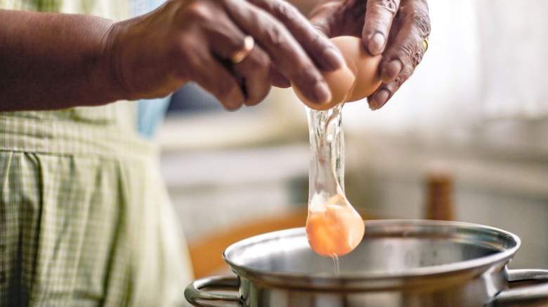 Hands crack a brown egg into a saucepan