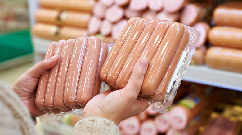 person holding hot dog packages in the store