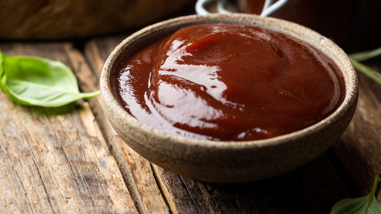 Bowl of barbecue sauce next to a basil leaf