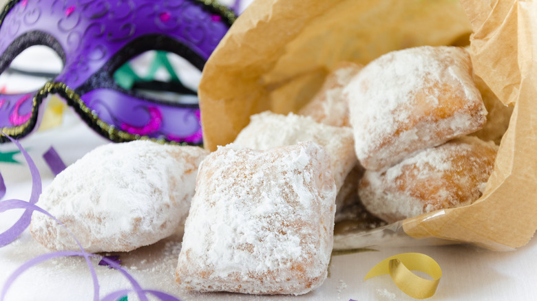 Bag of beignets next to a Carnival mask