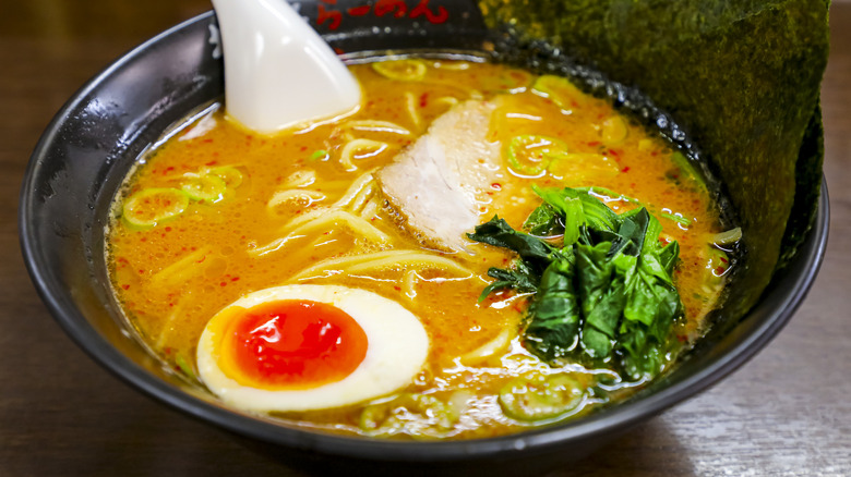 A bowl of savory ramen containing pork, greens, and a jammy egg