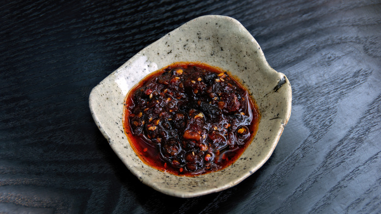 A stone bowl of chili crisp sits on a dark wooden surface