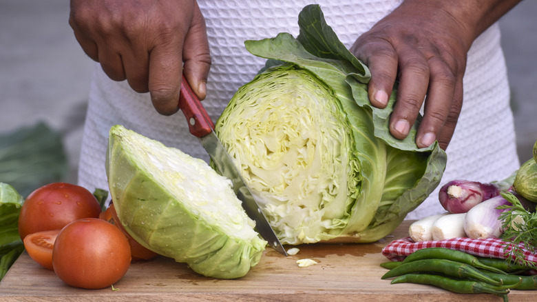 hands chopping a green cabbage on a cutting board