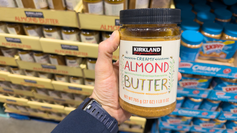 A hand holds a jar of Kirkland-branded almond butter.