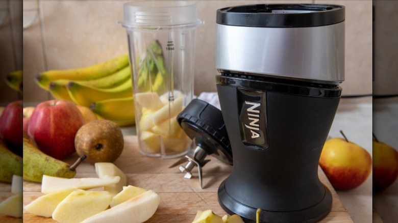 A Ninja personal juicer sits on a wooden cutting board amongst various fruits