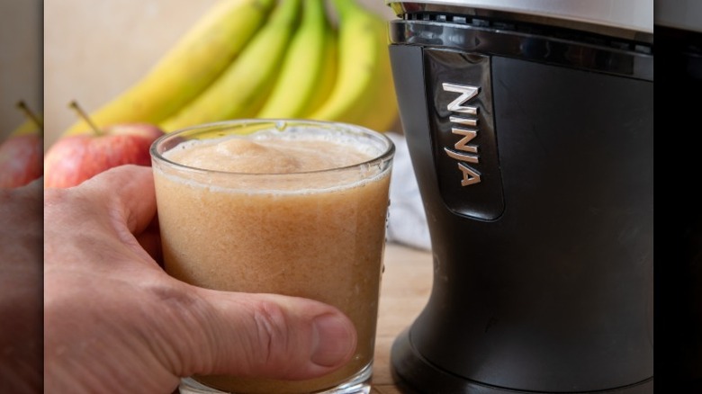 A person holds a glass of fresh juice next to a Ninja juicer