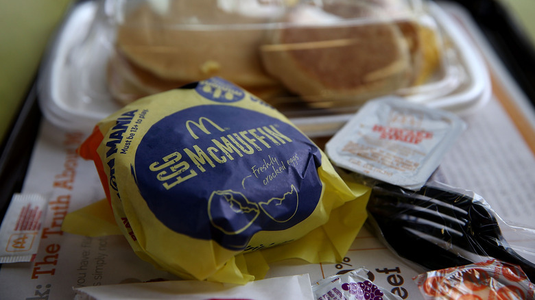 A wrapped up egg McMuffin with pancakes in the background.
