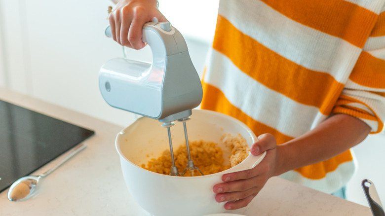 A person using an electric mixer to beat cookie dough