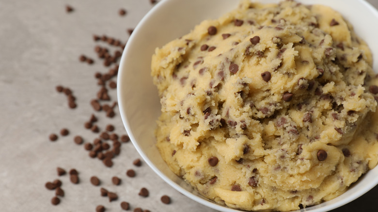 A white bowl full of cookie dough with chocolate chips on the table in the background