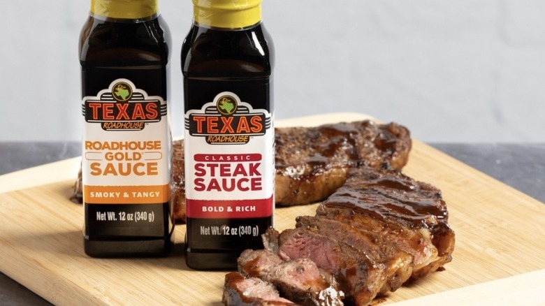 Bottles of Texas Roadhouse steak sauce beside a sliced steak on a cutting board