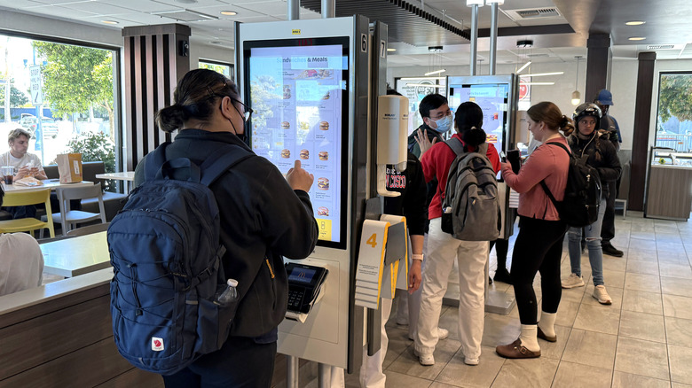 A line of customers orders at different fast food kiosks