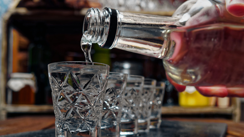 Bottle of vodka pouring into shot glasses