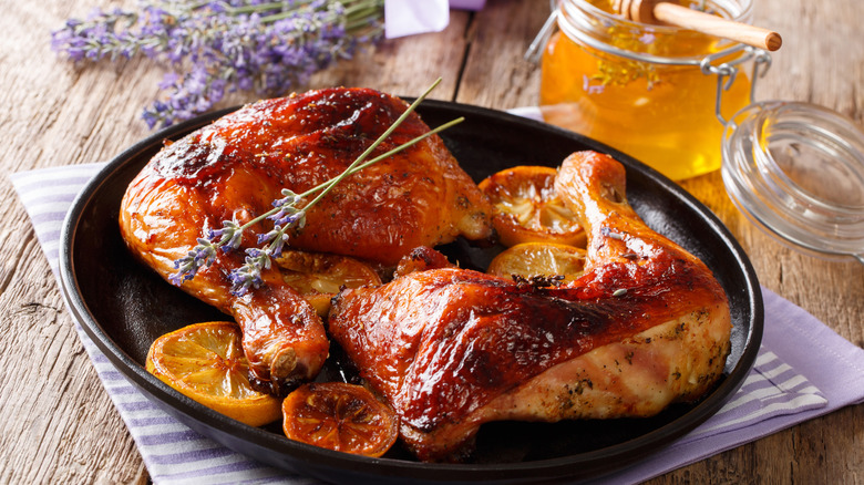Prepared chicken legs and thighs served with roasted lemon, honey, and lavender on plate.