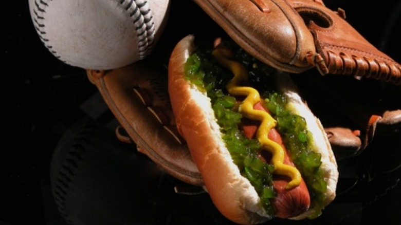 A hot dog covered in mustard and relish next to a baseball and mitt