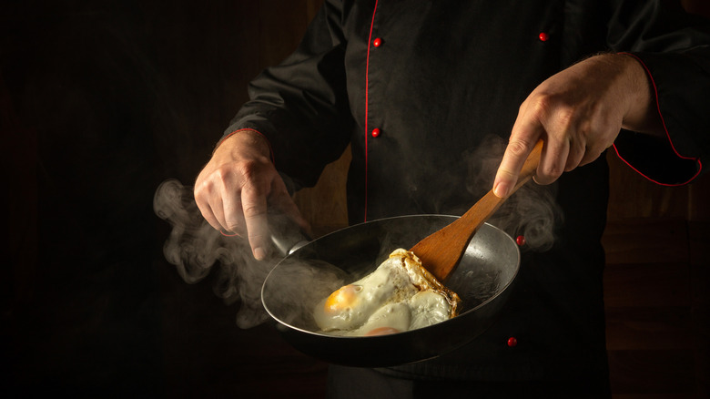 A chef flips two fried eggs with a wooden spatula