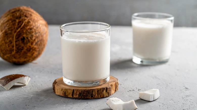 two glasses of coconut milk on wooden coasters with a coconut in the background