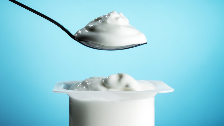 Container of yogurt with spoonful of yogurt above