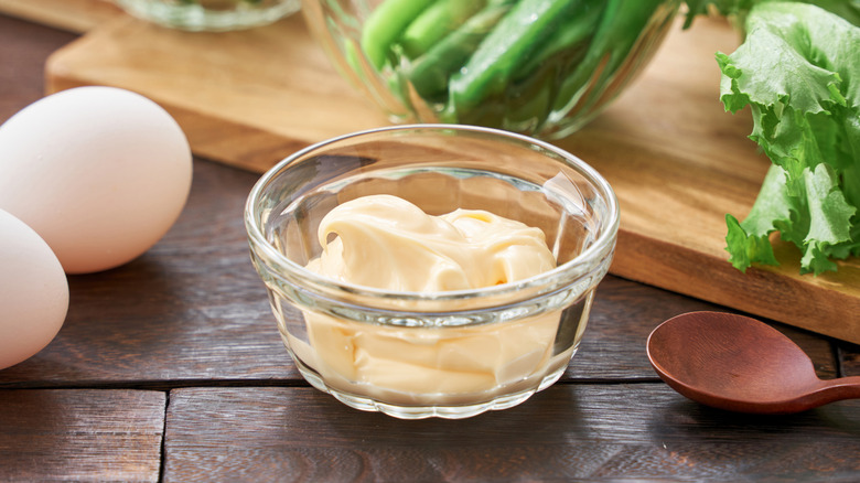 A small glass jar containing mayo next to eggs and a wooden spoon.
