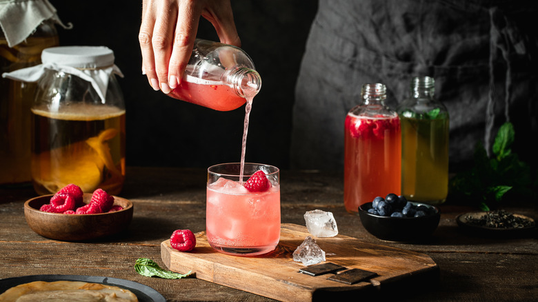 person pouring kombucha into glass cup