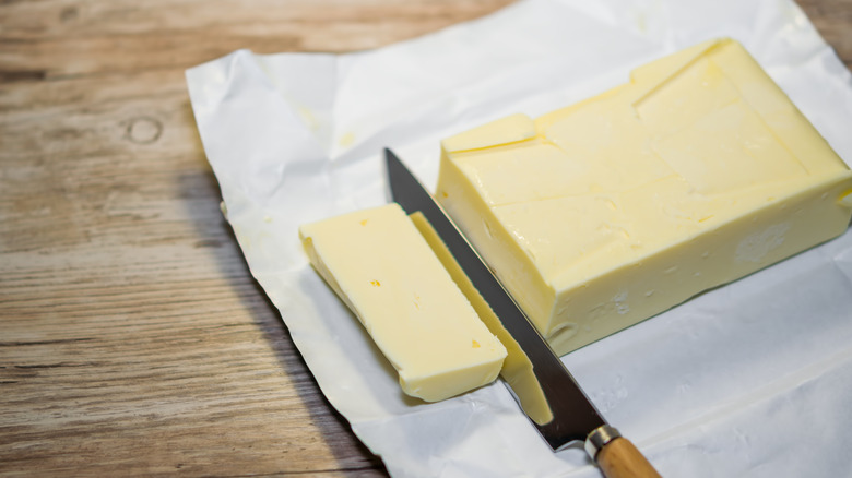 A knife cuts through a block of butter on its opened foil wrapping