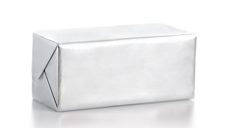 A foil-wrapped rectangle of butter sits against a white background