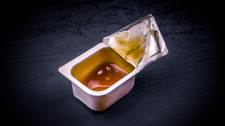 Open sauce packet on black background.