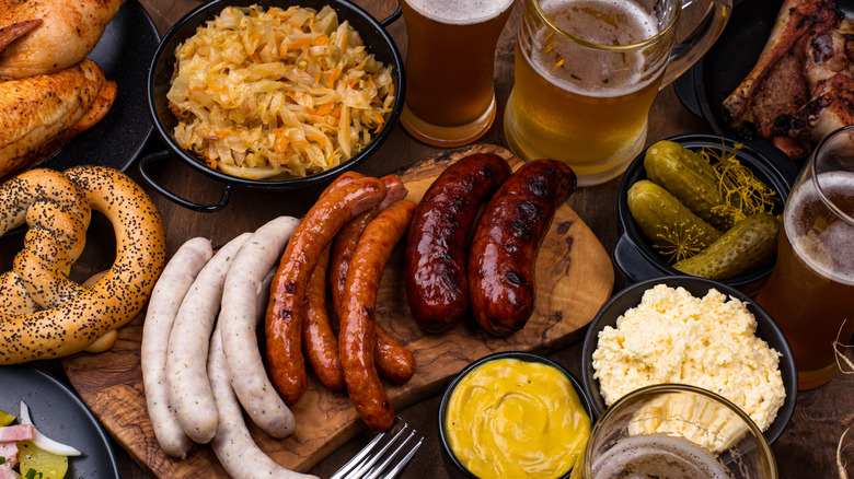 Cooked bratwurst with sauerkraut, mustard, pickles, potato salad, pretzels, and beer