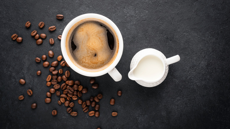 A cup of coffee with a jug of creamer 