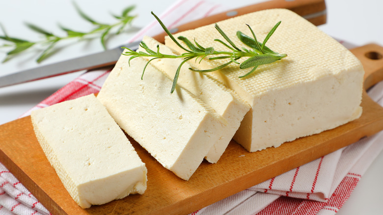 Sliced block of tofu with herbs on wood cutting board