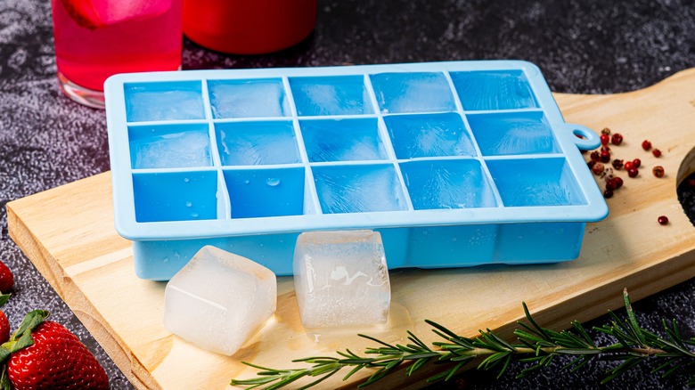 Frozen ice cubes and blue ice tray on wooden cutting board