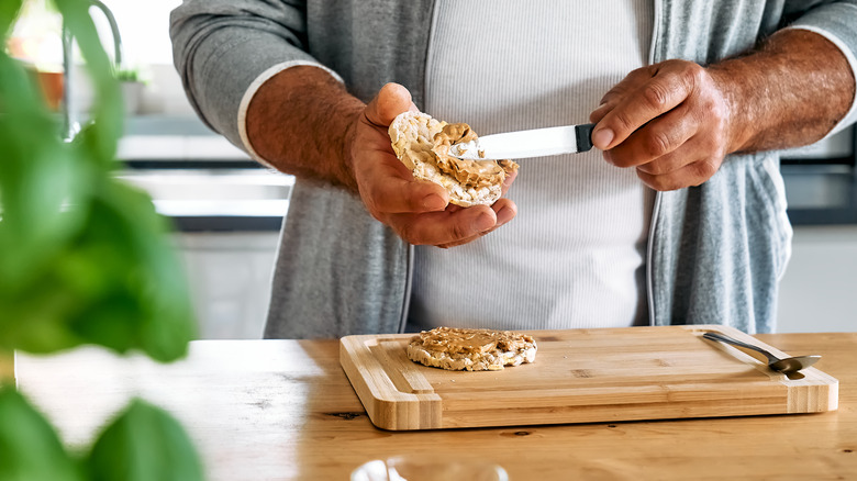 man spreading peanut butter on rice cake
