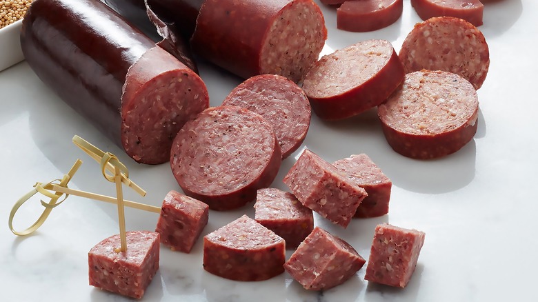 Summer sausage encased in maroon-colored parchment paper sliced into thick triangles and served with toothpicks