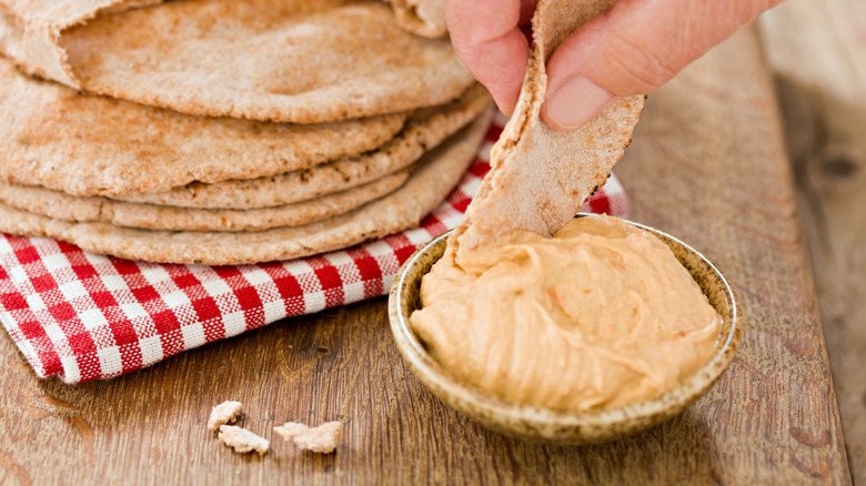 person dipping pita bread into small hummus container