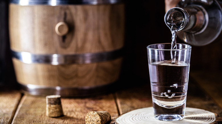 Pouring tequila in shot glass from bottle near barrel