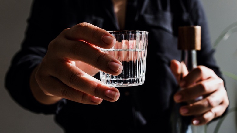 Glass of clear spirit in hand with bottle