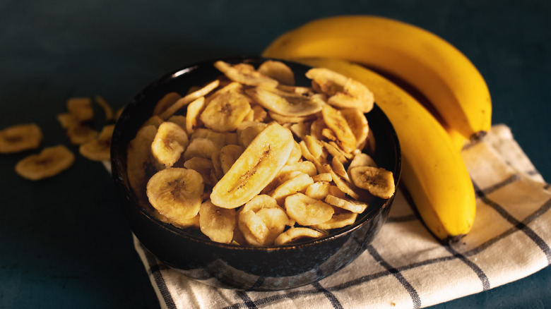 Banana chips in black bowl next to whole bananas