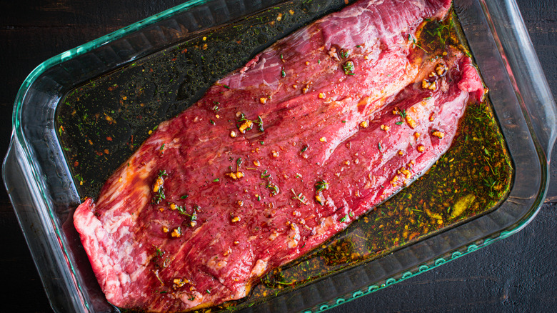 Raw steak marinating in glass dish