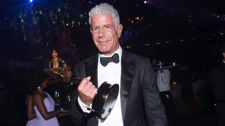 Anthony Bourdain holding an award in a suit