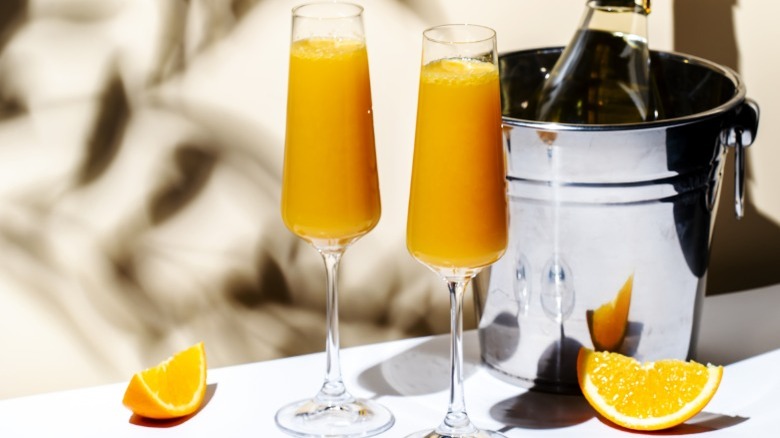 Two mimosas in front of a bucket and champagne bottle 