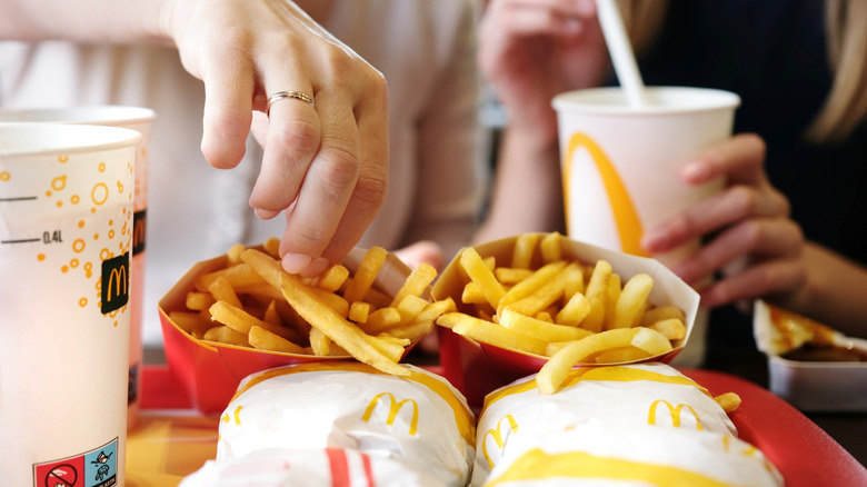Two customers eat McDonald's french fries from a tray also containing burgers and drinks
