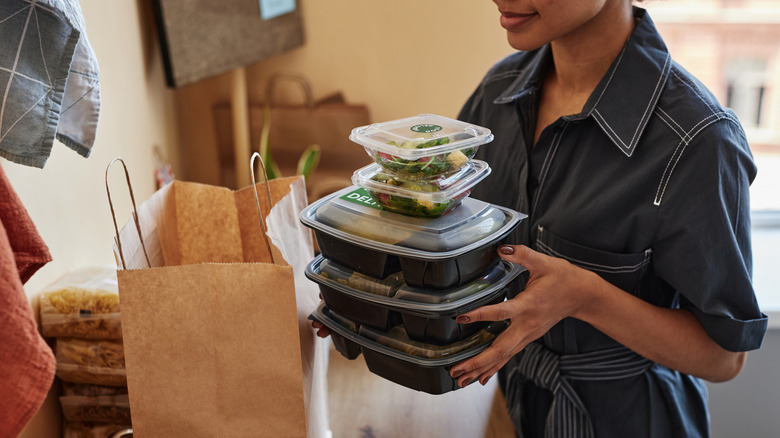 A person holding several full plastic takeout containers.