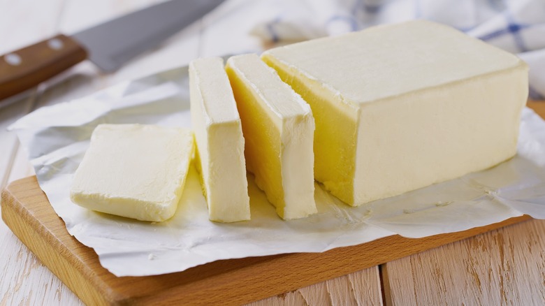 stick of butter is sliced on a wooden block