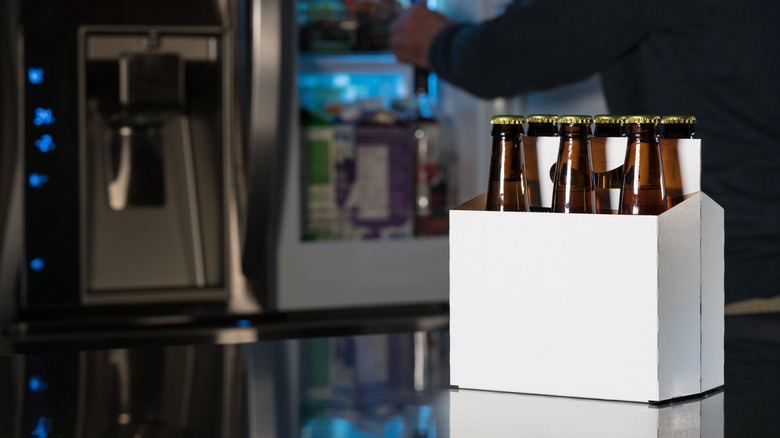 A six-pack of beer displayed next to a fridge.