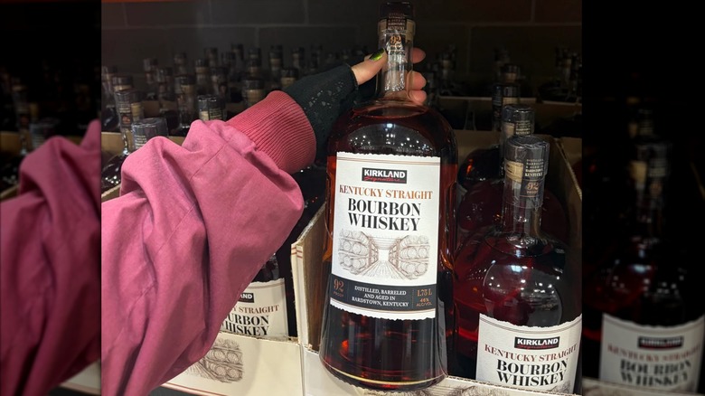 A shelf of bottles of Kirkland Kentucky Straight Bourbon Whiskey , as well as one bottle held, sold at Costco.