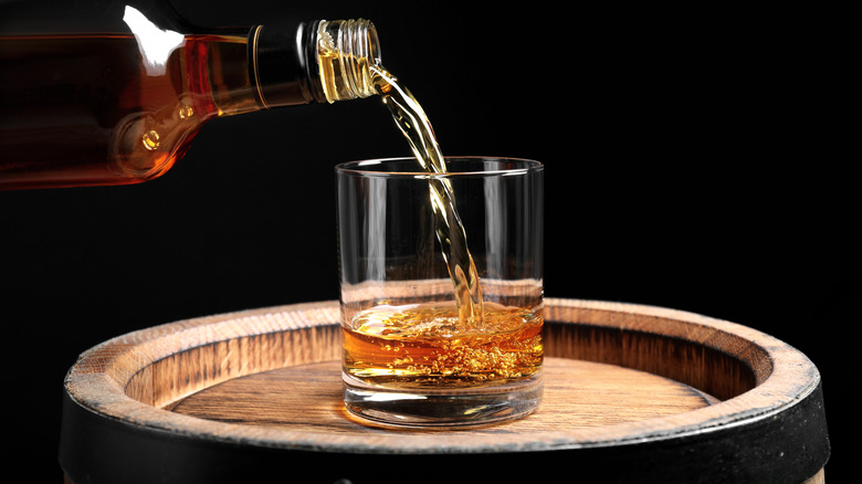 Bottle of whiskey being poured into glass on a barrel